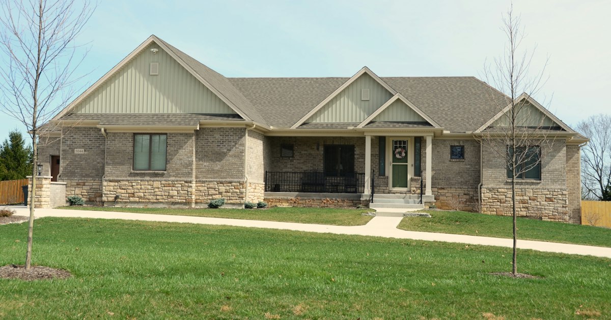 Single-story stone and brick house with a wide lawn
